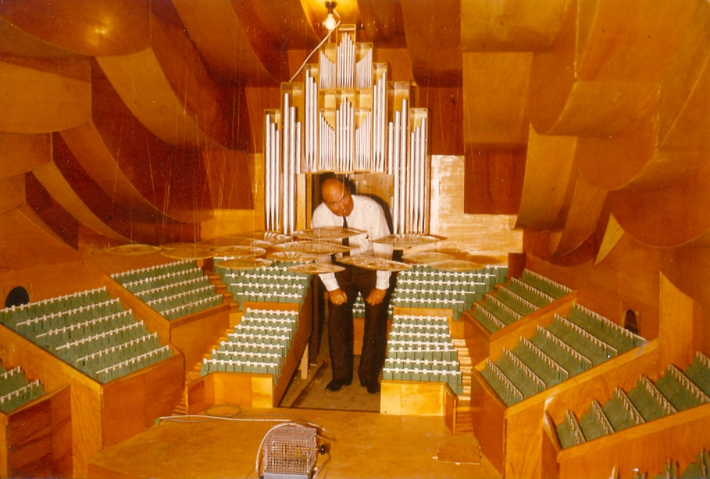 A man stooping under the organ of a large scale model of the Concert Hall, looking at the perspex discs.