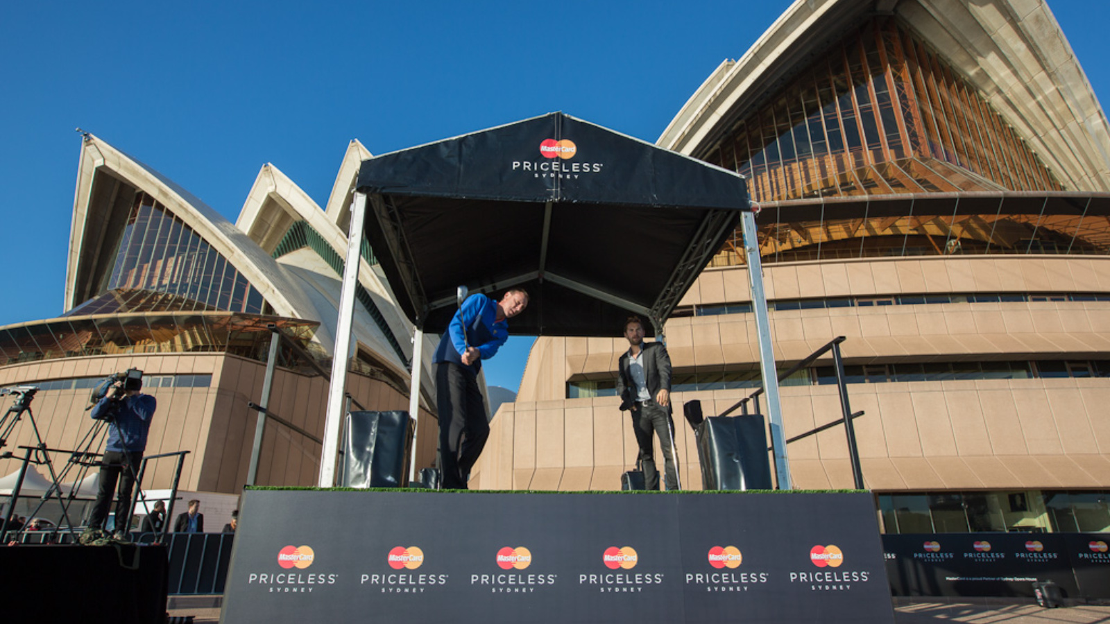 Two men playing golf under a Mastercard stand outside the Sydney Opera House.