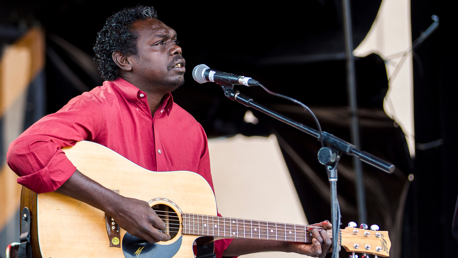 A man playing a guitar while singing in to a mic.