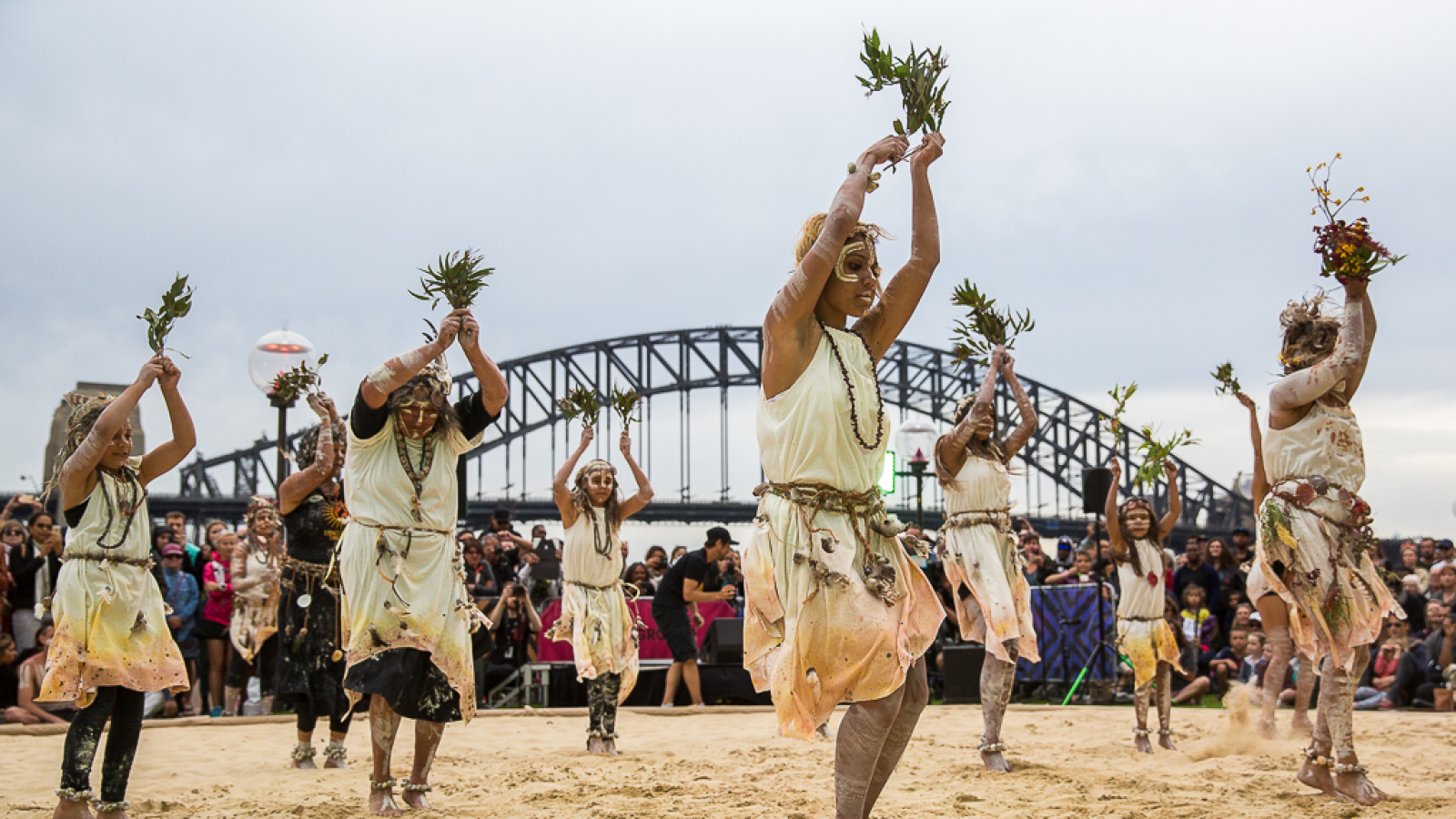 Women in sand pit performing indigenous dance in the Homeground of Sydney opera house.
