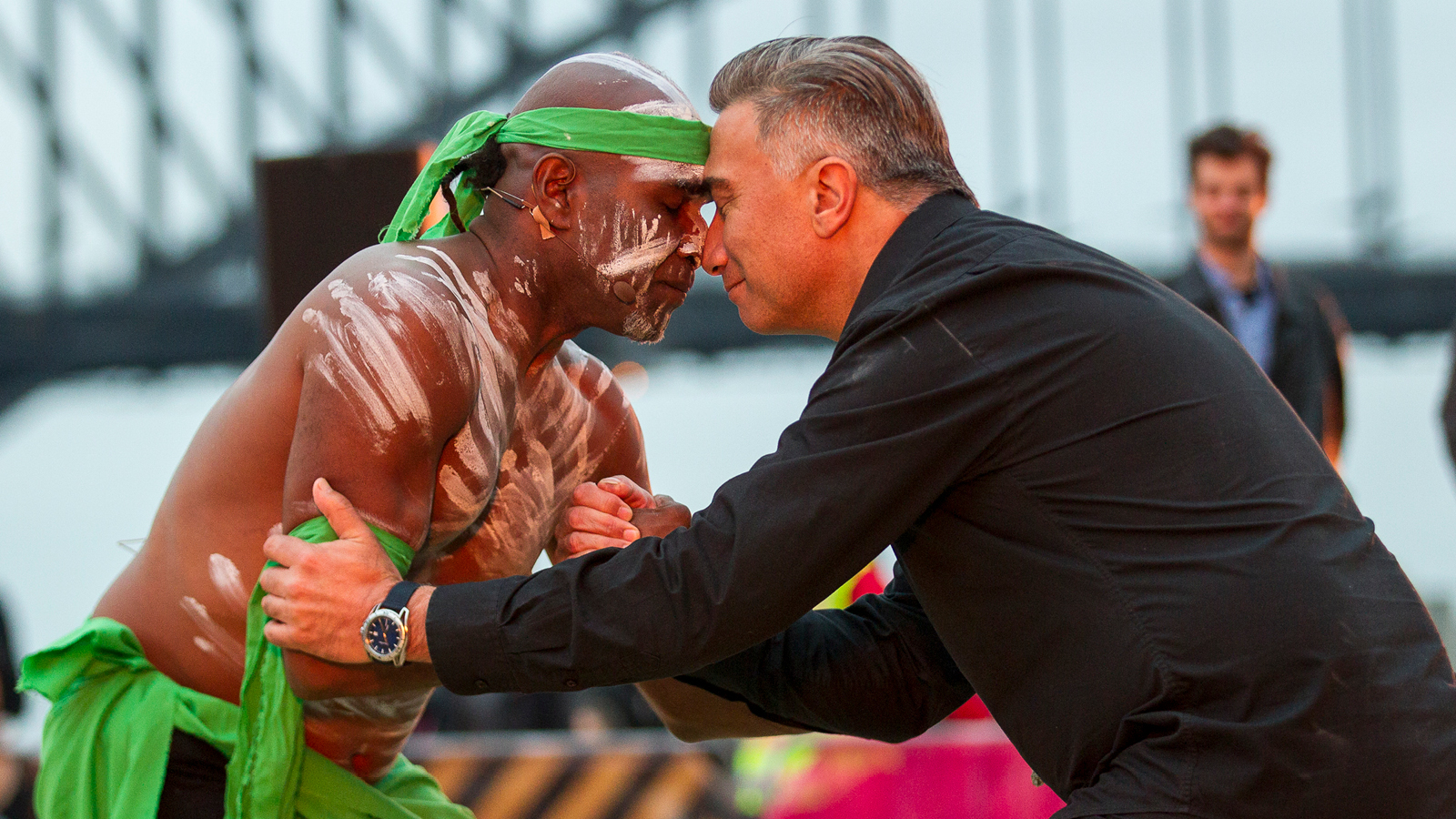 An Aboriginal man and a man touching each other with their foreheads and holding hands.