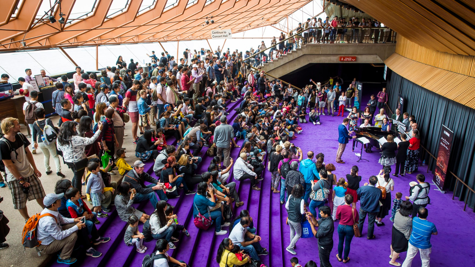 A crowd of people sitting on purple steps inside the Sydney Opera House.