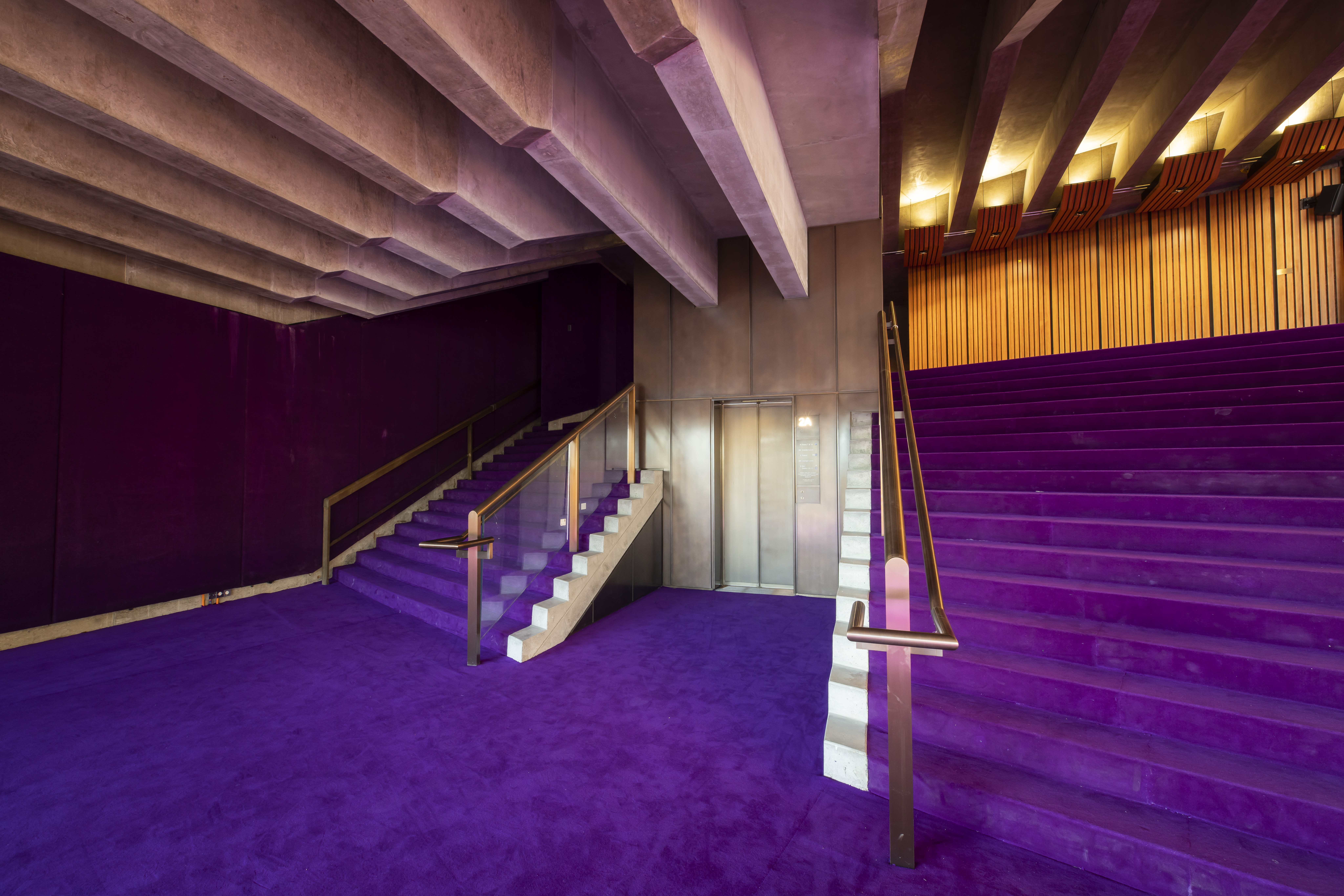 A lift and two staircases beside it with purple carpet.