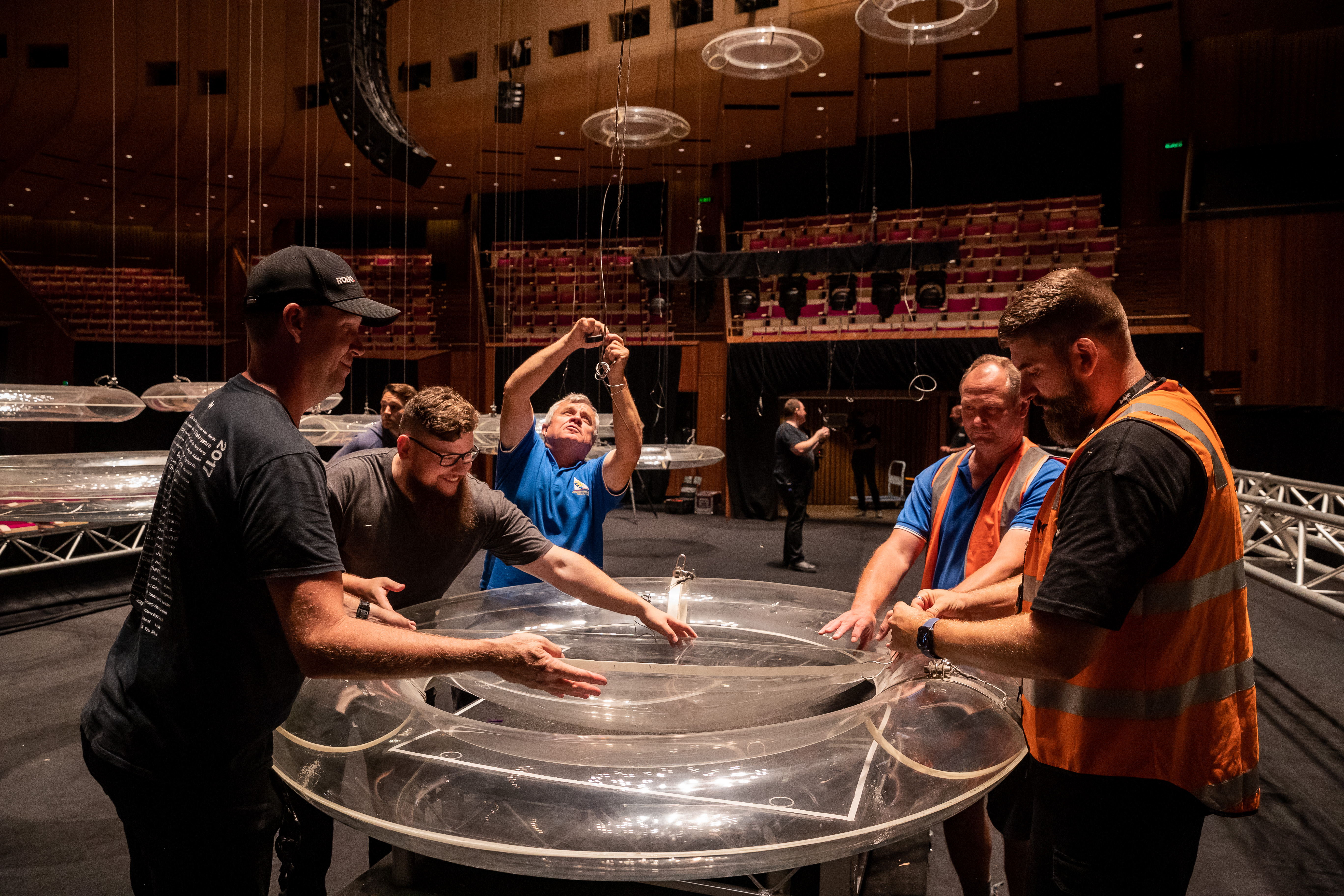 A group of people standing around a perspex disc in the Concert Hall, removing strings from it.
