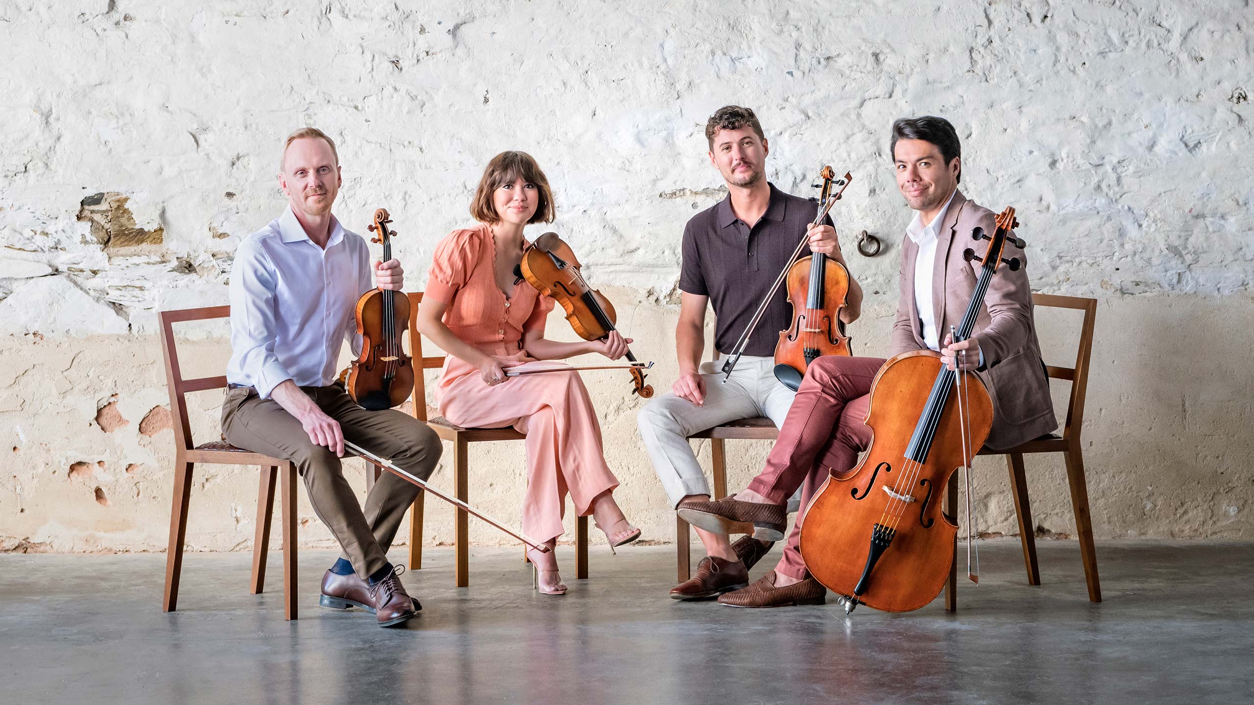 A string quartet holds their instruments looking at the camera