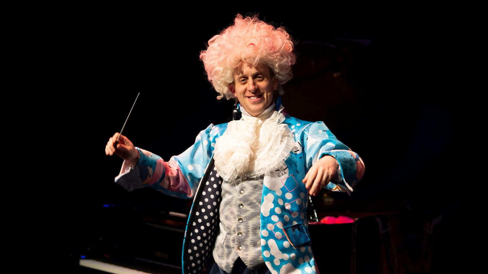 A man and woman dressed up as Mozart and his wife in colourful outfits and big white wigs