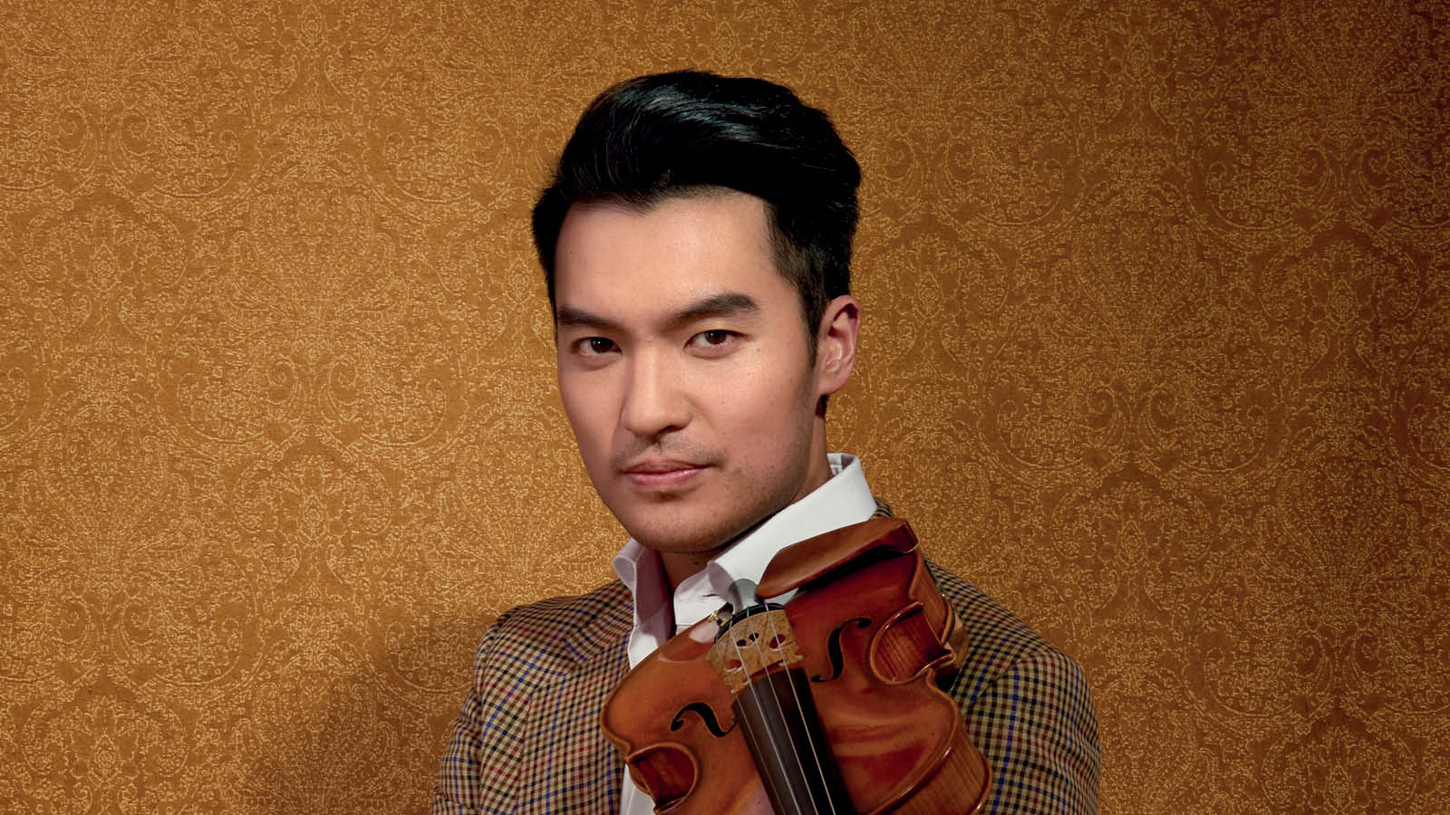 A man a brown suit holding a violin.