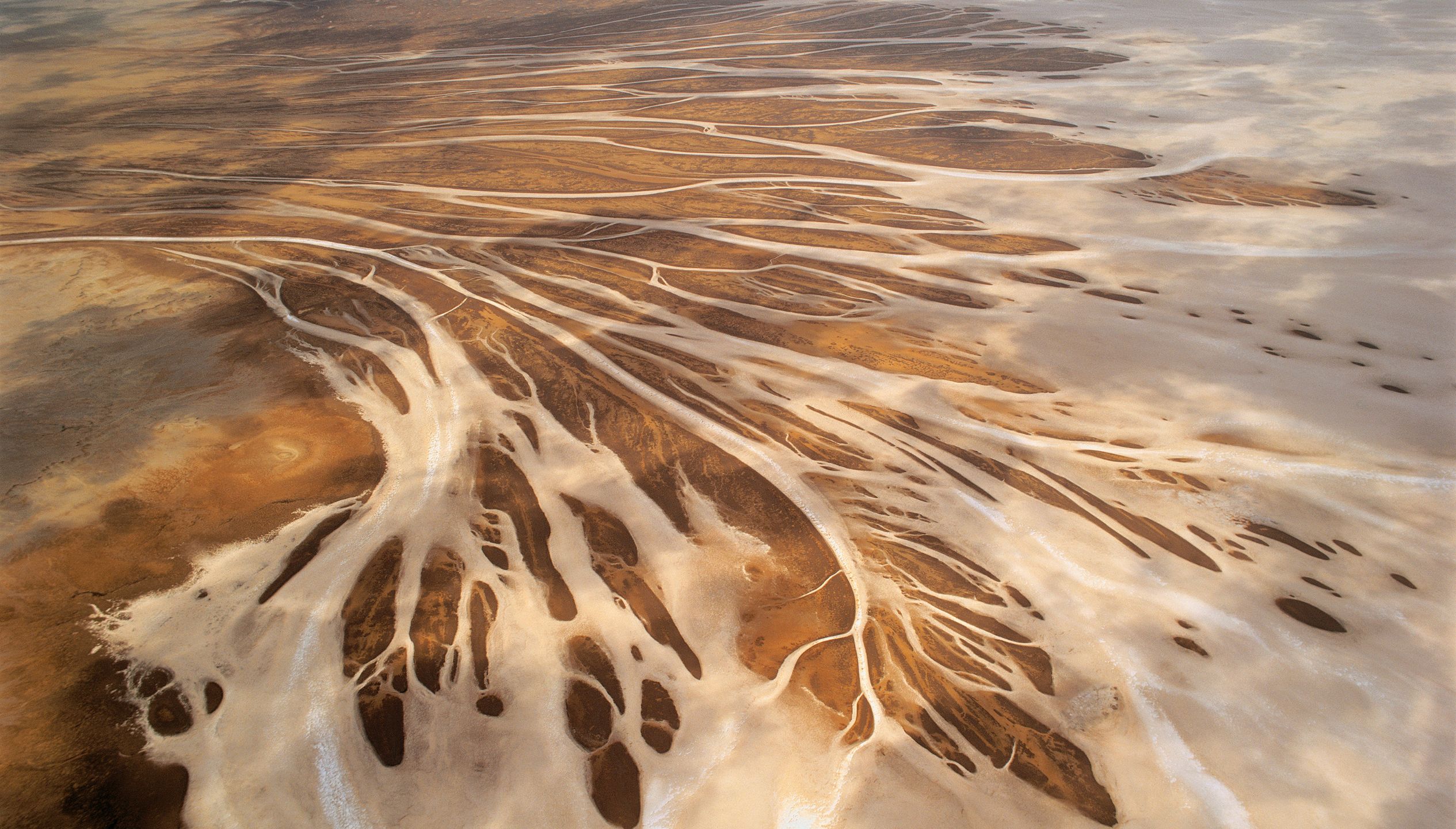 A very wide bird's eye view of empty brown arid land with river systems zip zagging through the land