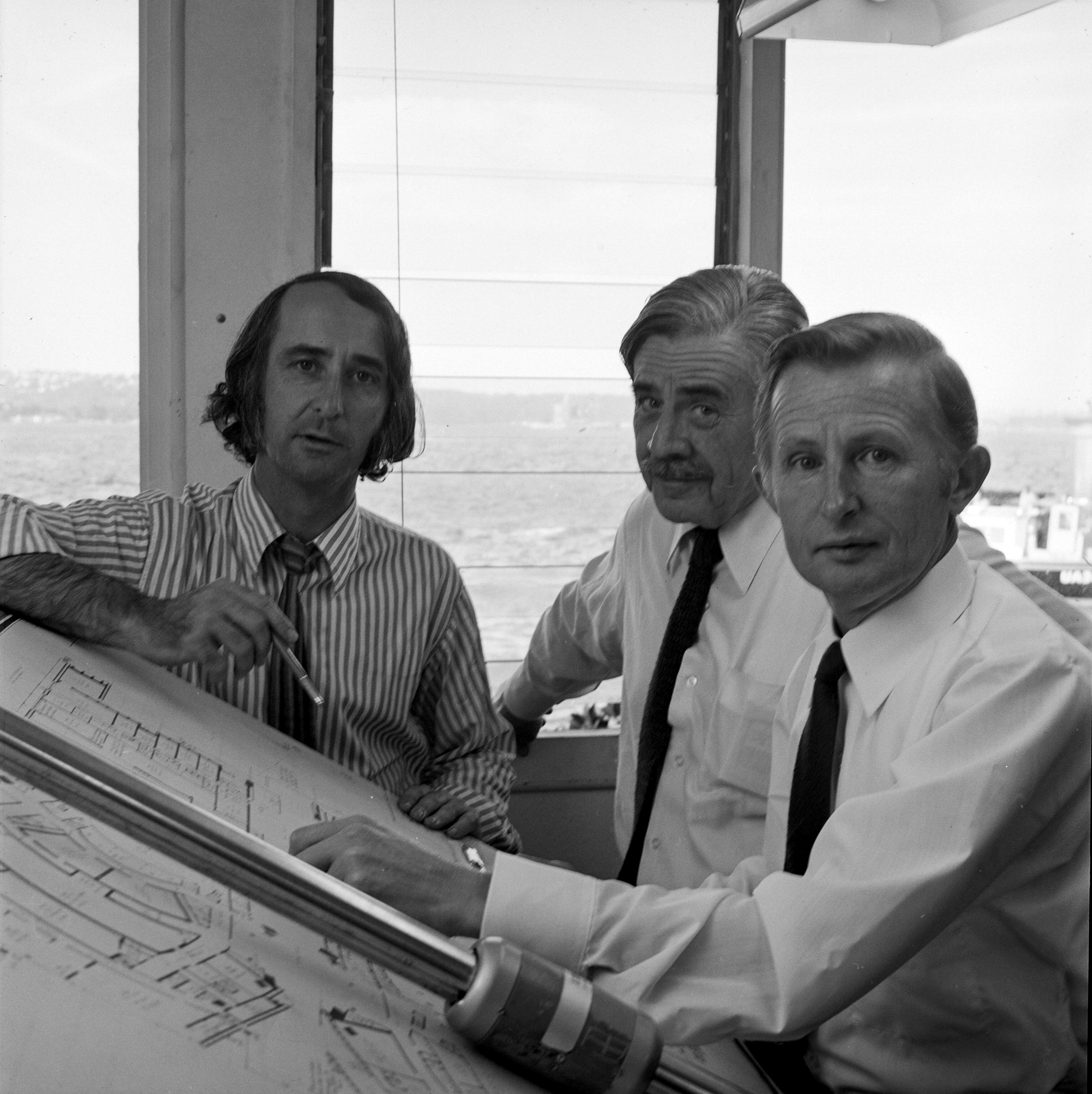 Three men sitting close to a drafting table.