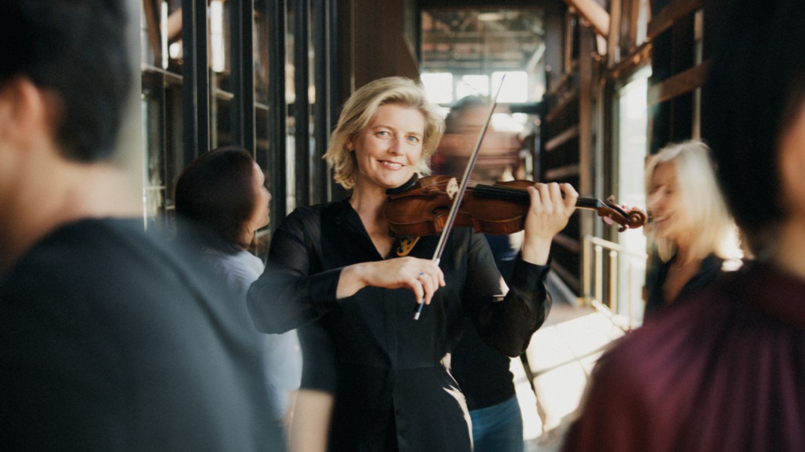 A woman playing a violin while people walk around her.