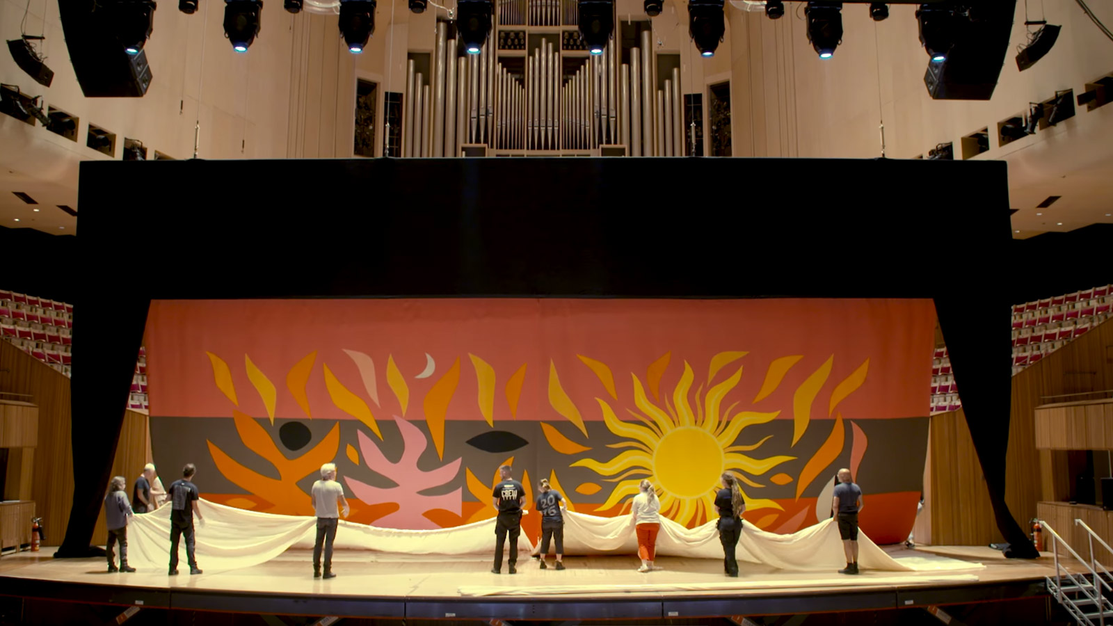 A team of men and women installing the tapestry curtain in the Concert hall.