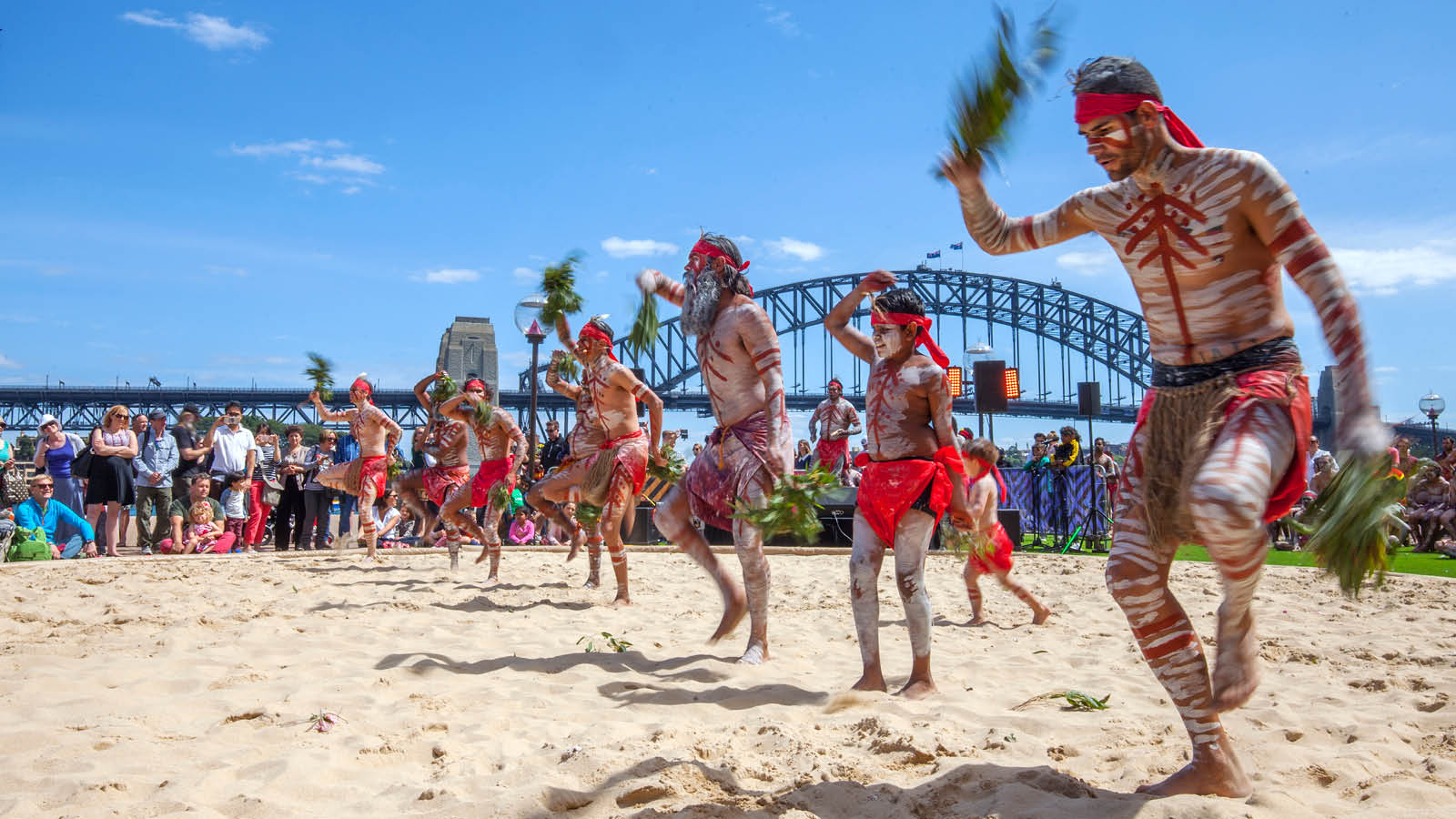 Men in sand pit performing indigenous dance in the homeground of Sydney opera house.