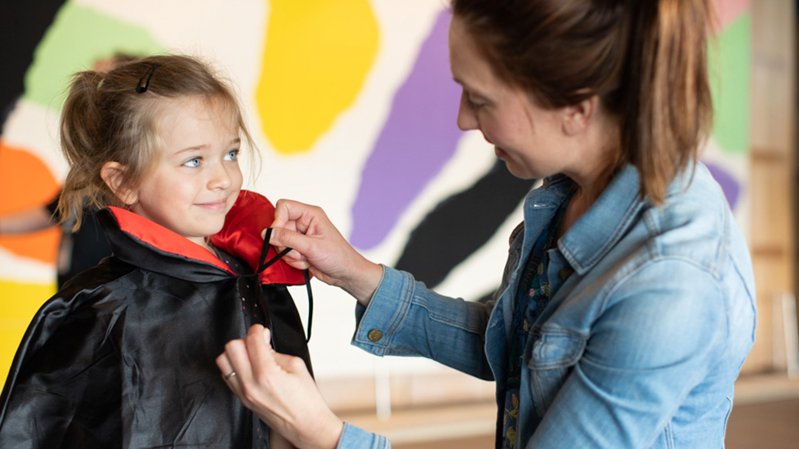 A woman tying a cape around a girl's neck.