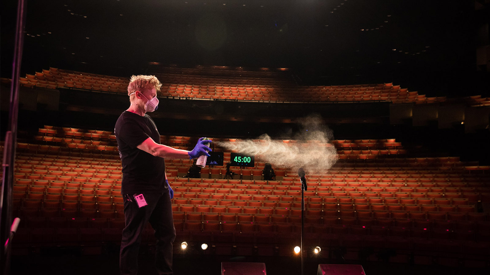 Man spraying aerosol into a microphone on stage.