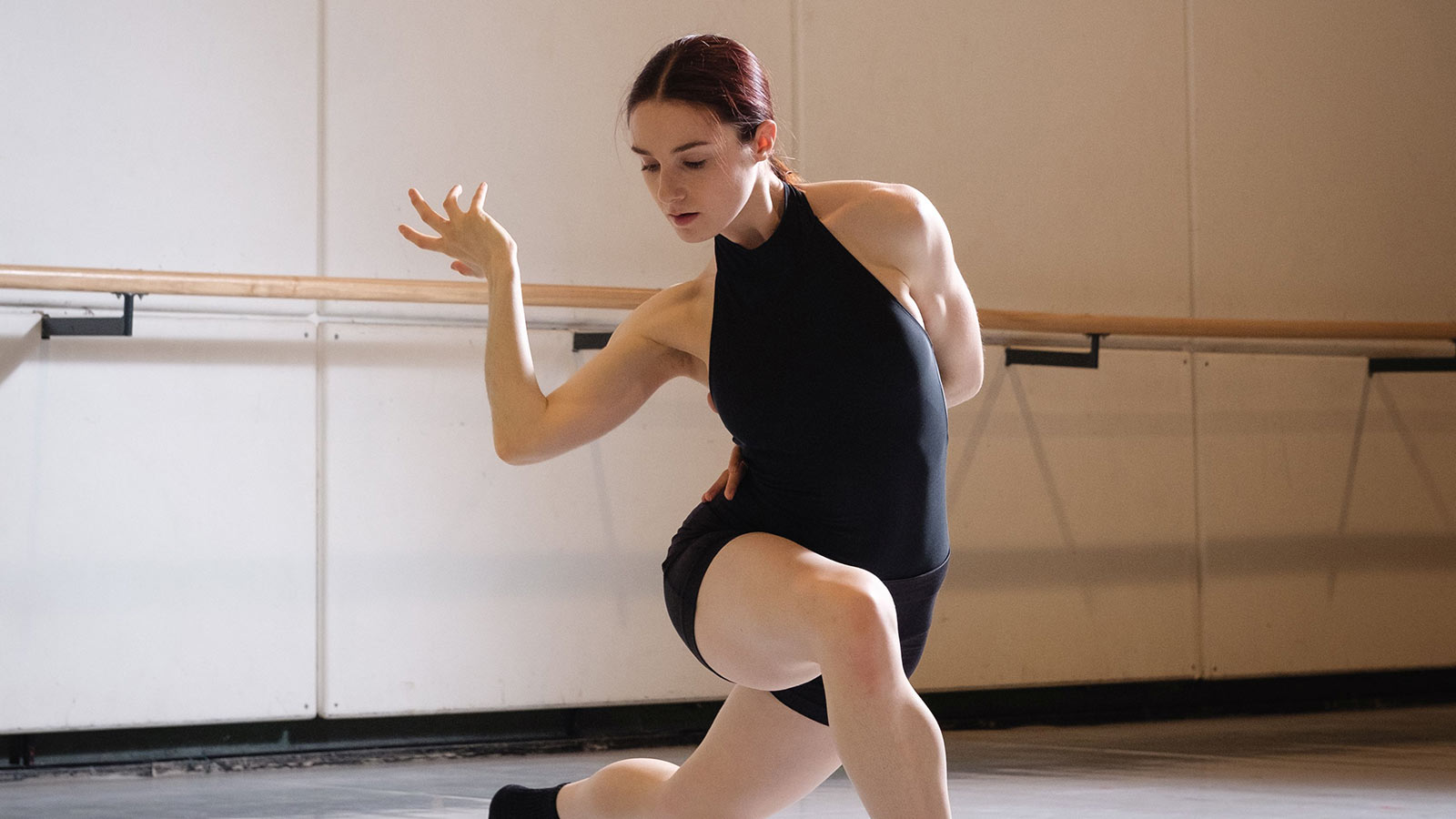 A woman in a black leotard dancing in a studio.