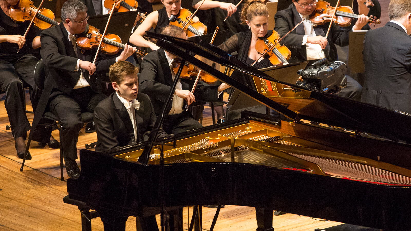 A man playing a grand piano in an orchestra.