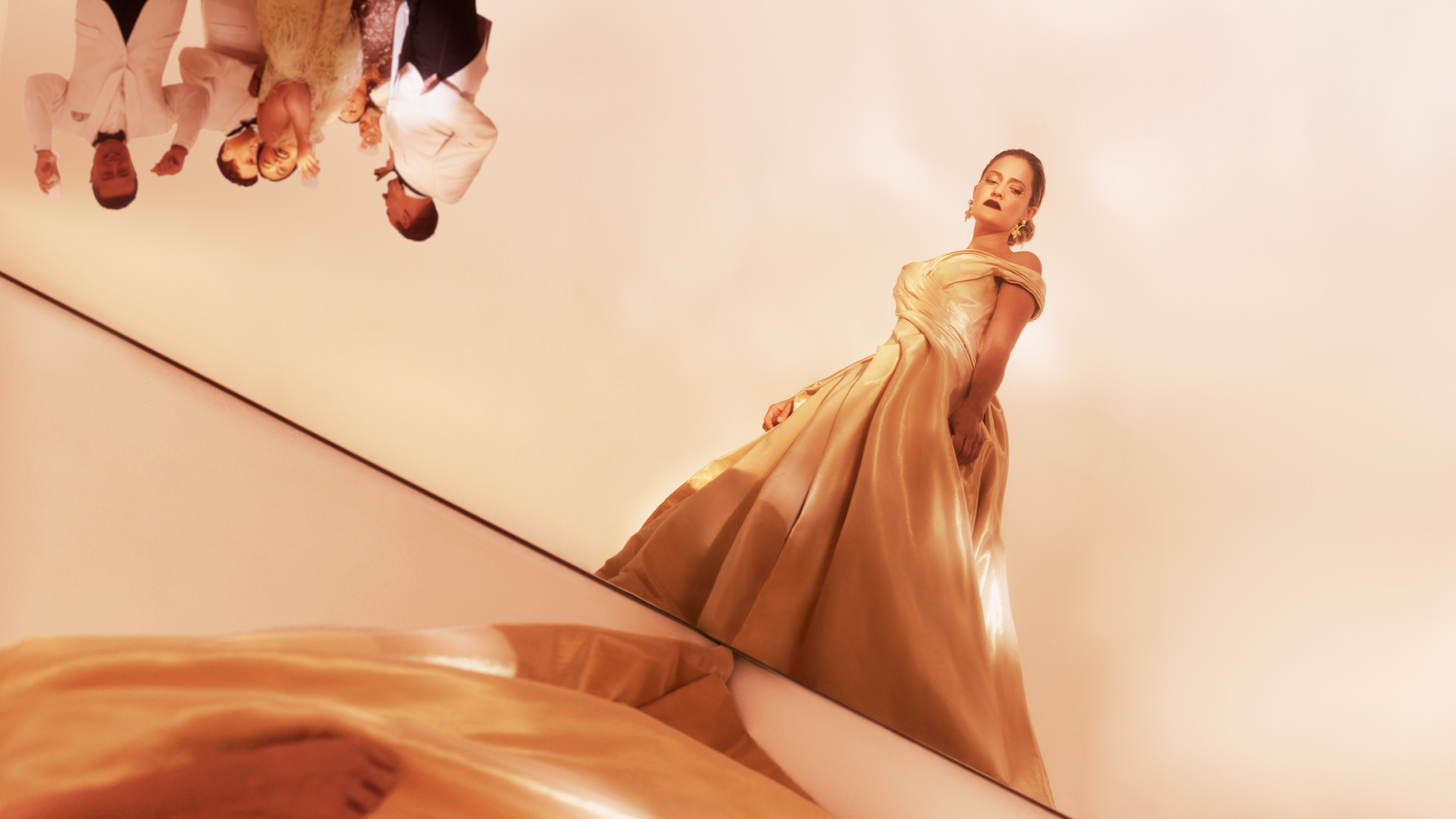 Woman in gold ballgown stands away from other partygoers