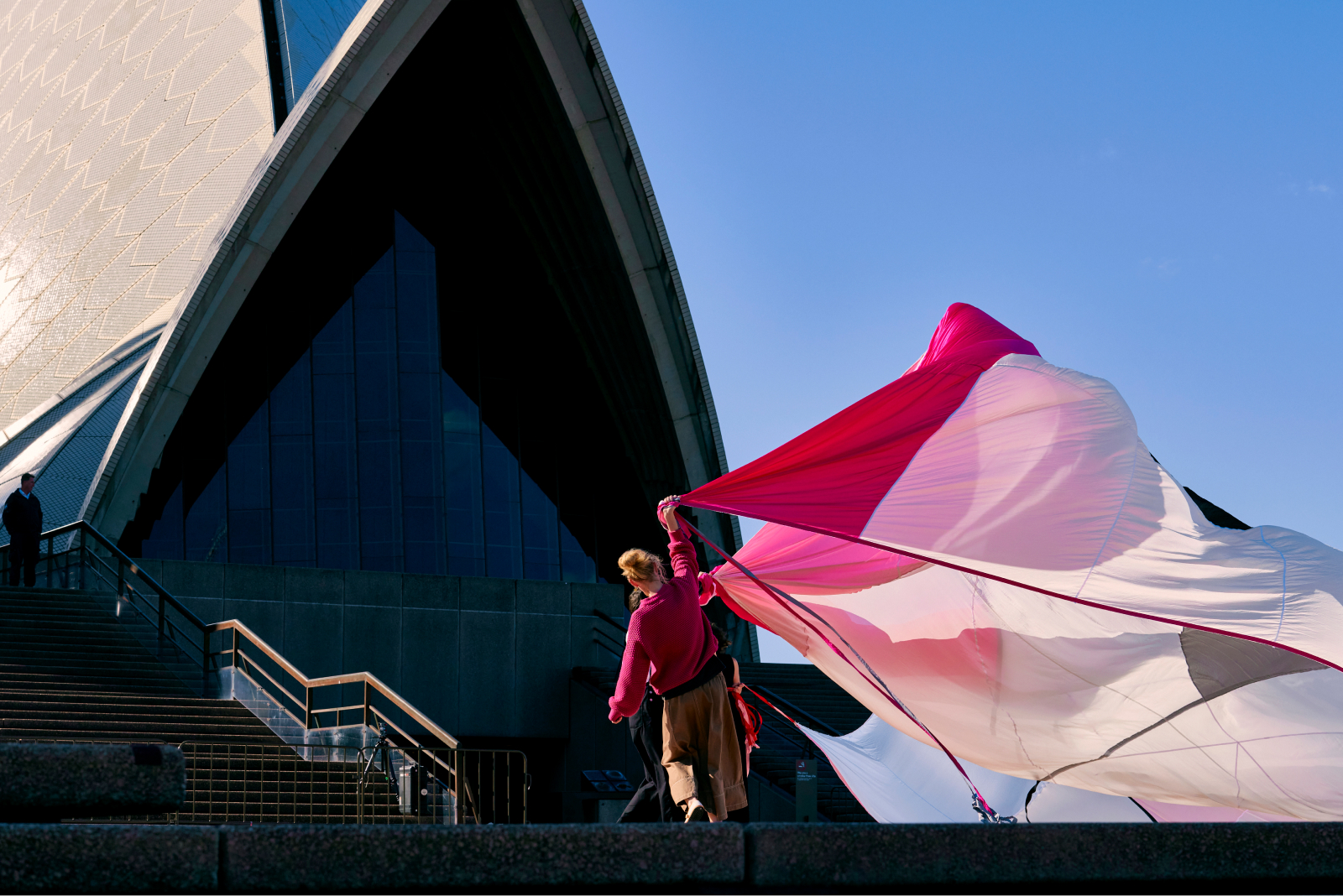 A woman outside Sydney opera house holding a long curtain.