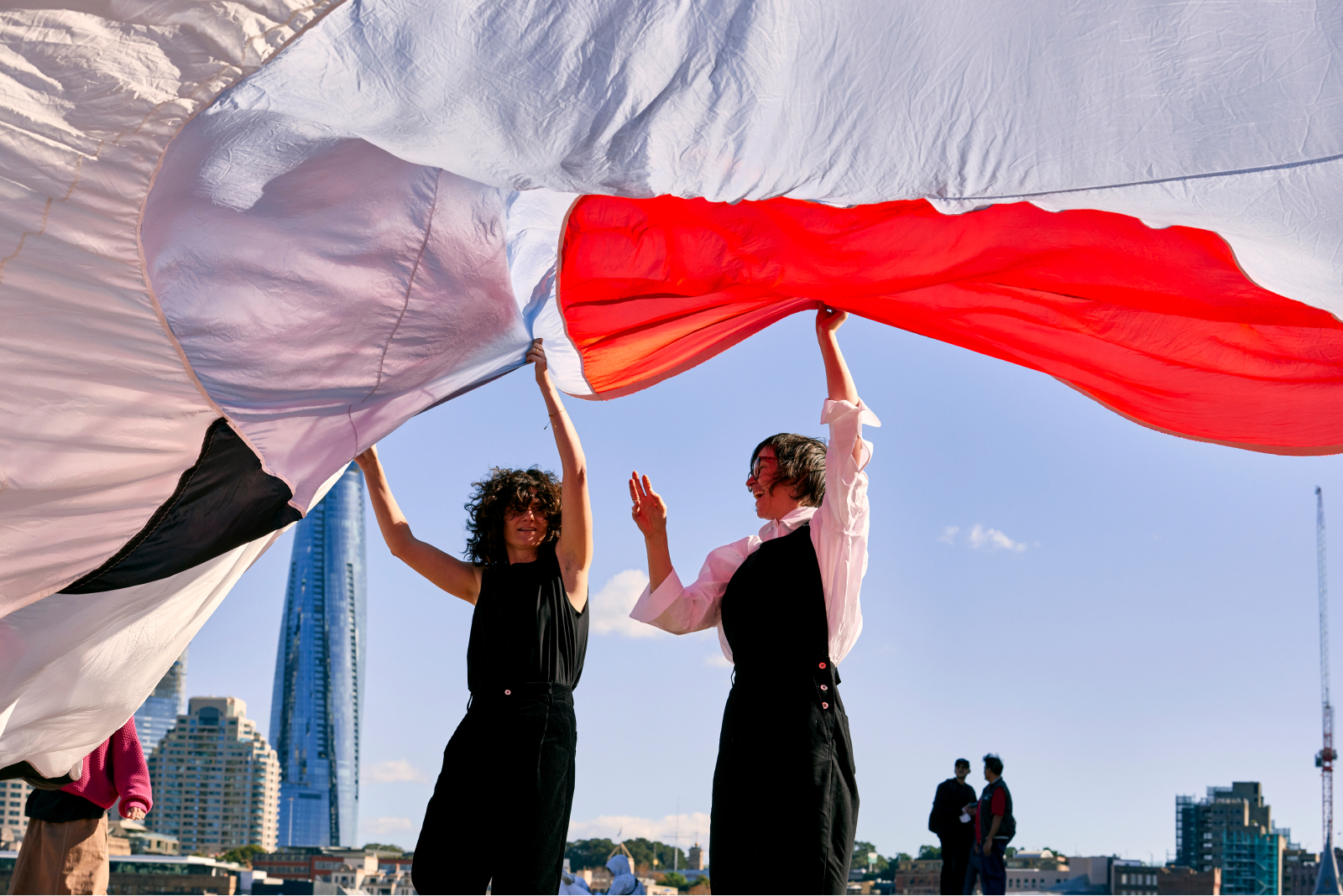 A man and a woman holding a long curtain outside Sydney opera house.