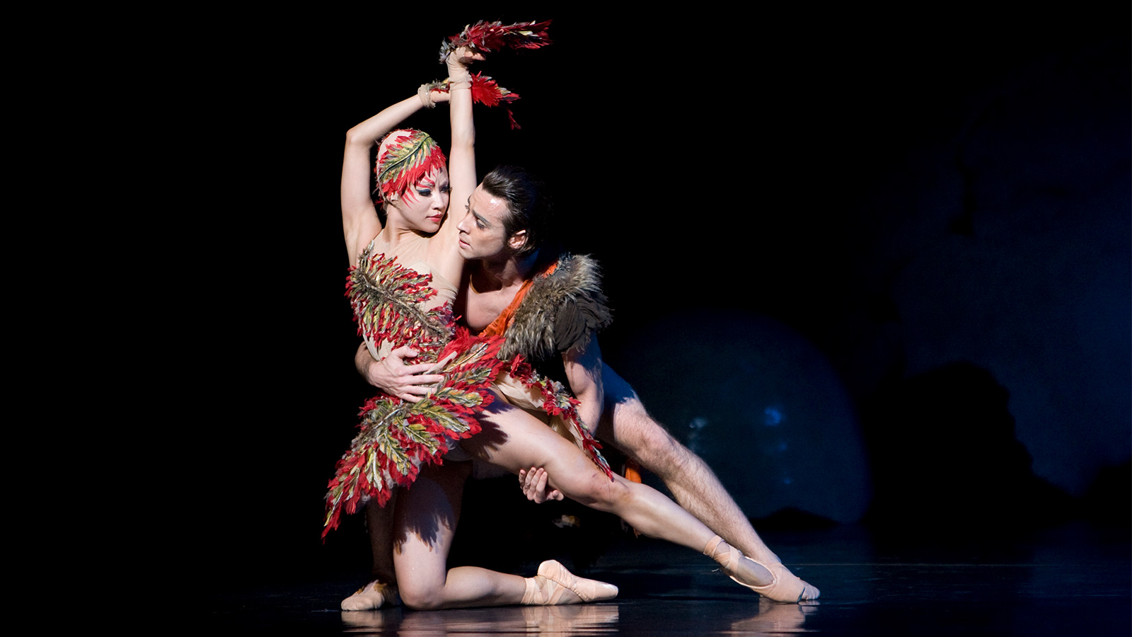 Two dancers, one in a red feathered costume.