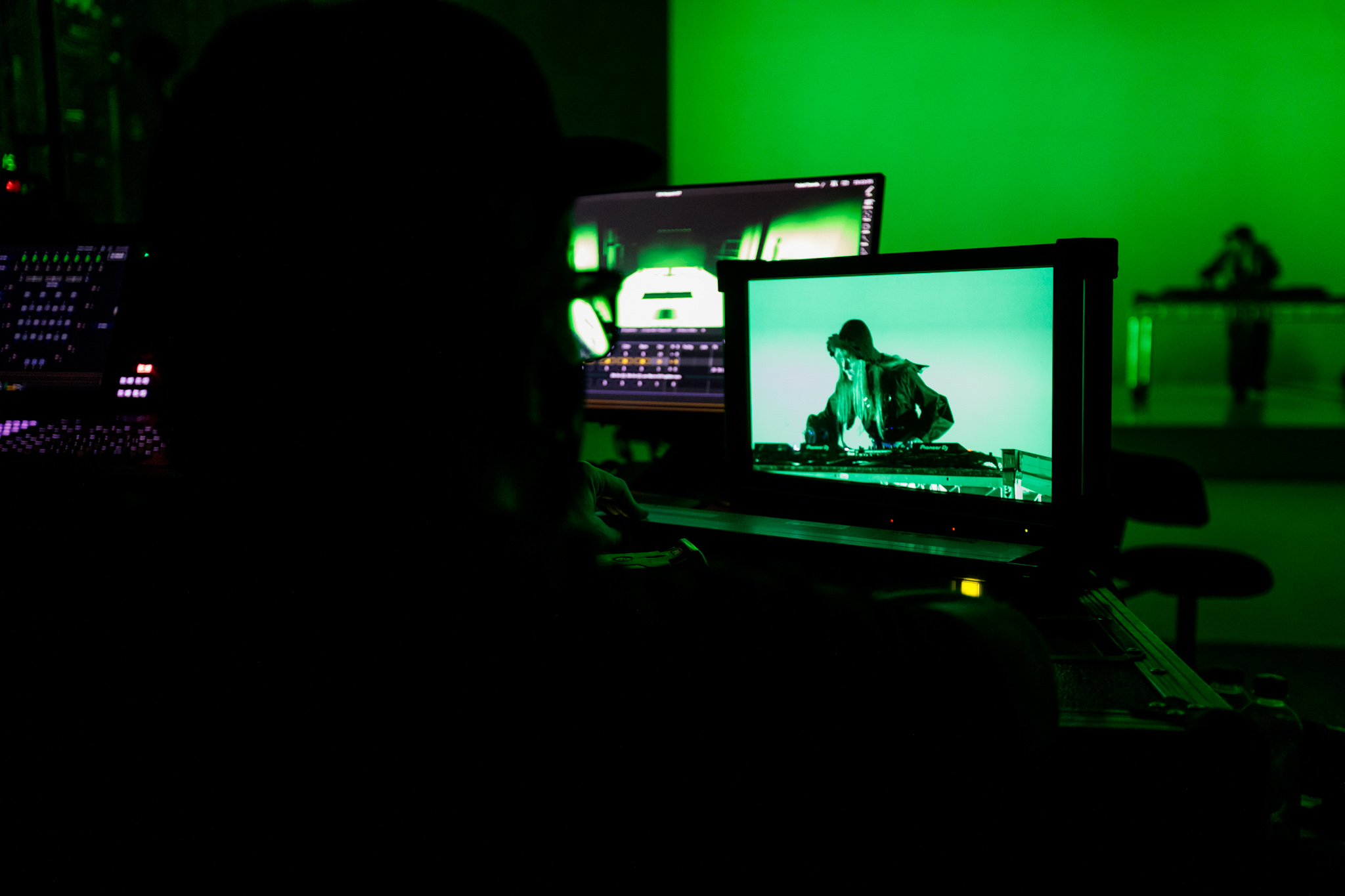 Producer's view through screens of a person standing over a deck in a recording room under a green light