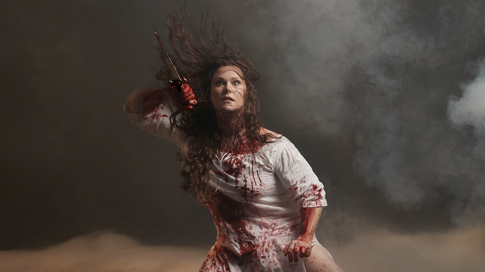 A woman holding a dagger and drenched with blood.