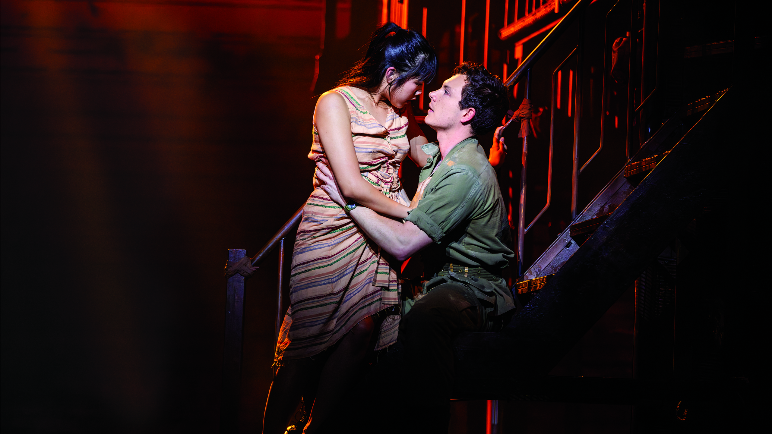 An Asian woman and a white man are perched on stairs holding each other lovingly.