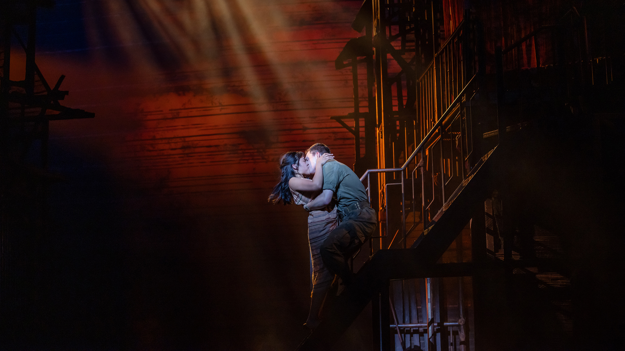An Asian woman and white man embrace and kiss on stairs.