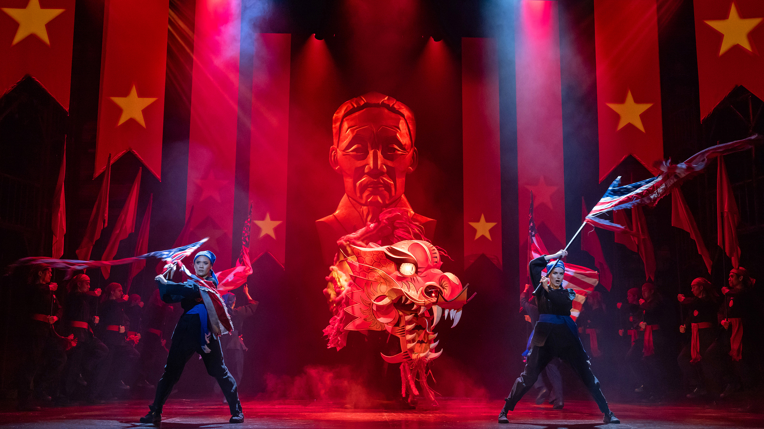 Two men wave American flags wearing a 1970s army uniform. A Chinese-style dragon is between them. Vietnamese flags can be seen behind them in an ominous scene.