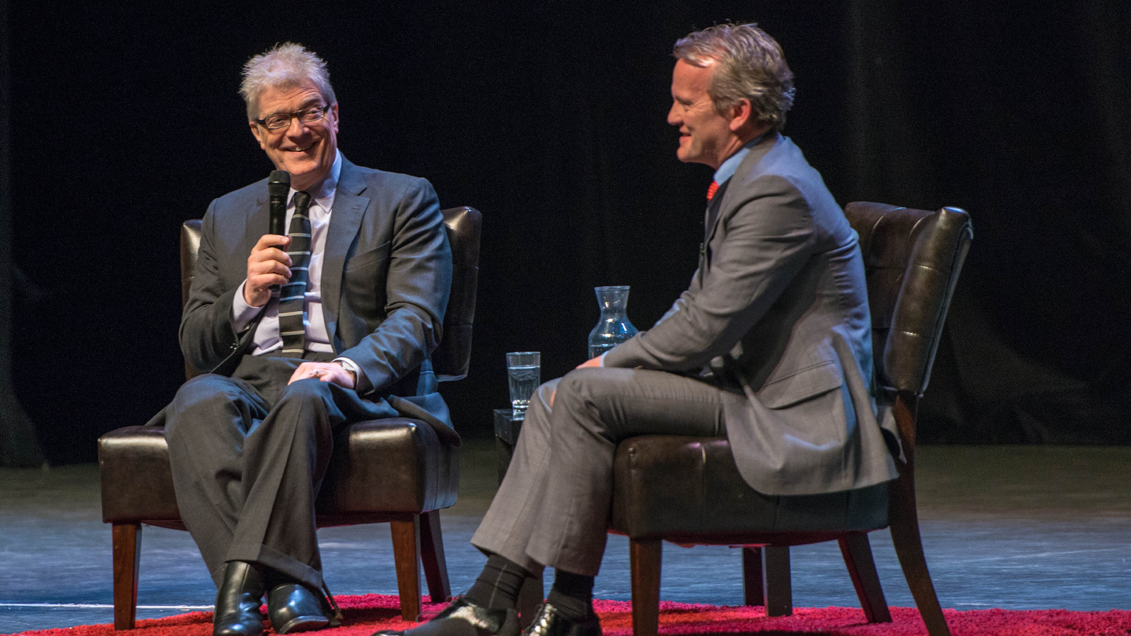 Two middle age men wearing suit, having a debate on the stage.