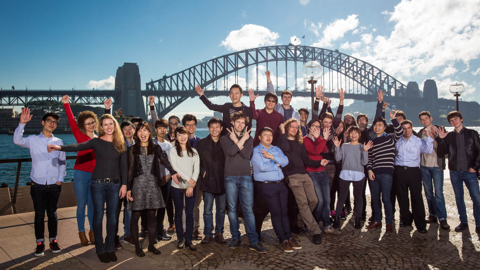 A group of people standing near Sydney opera house with Harbour bridge in the background.