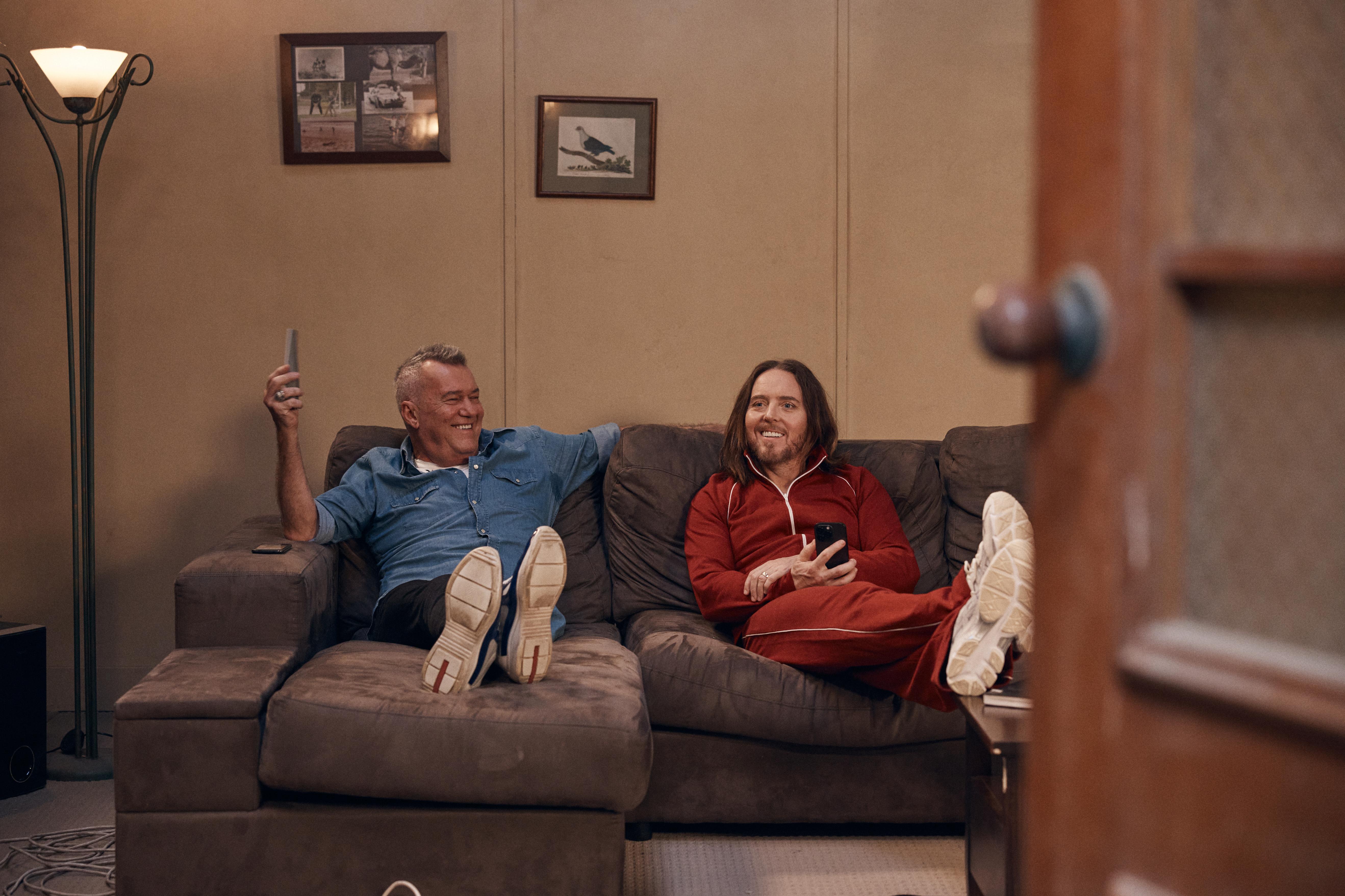 Two people sitting in a living room with their feet up. One holding a tv remote control.