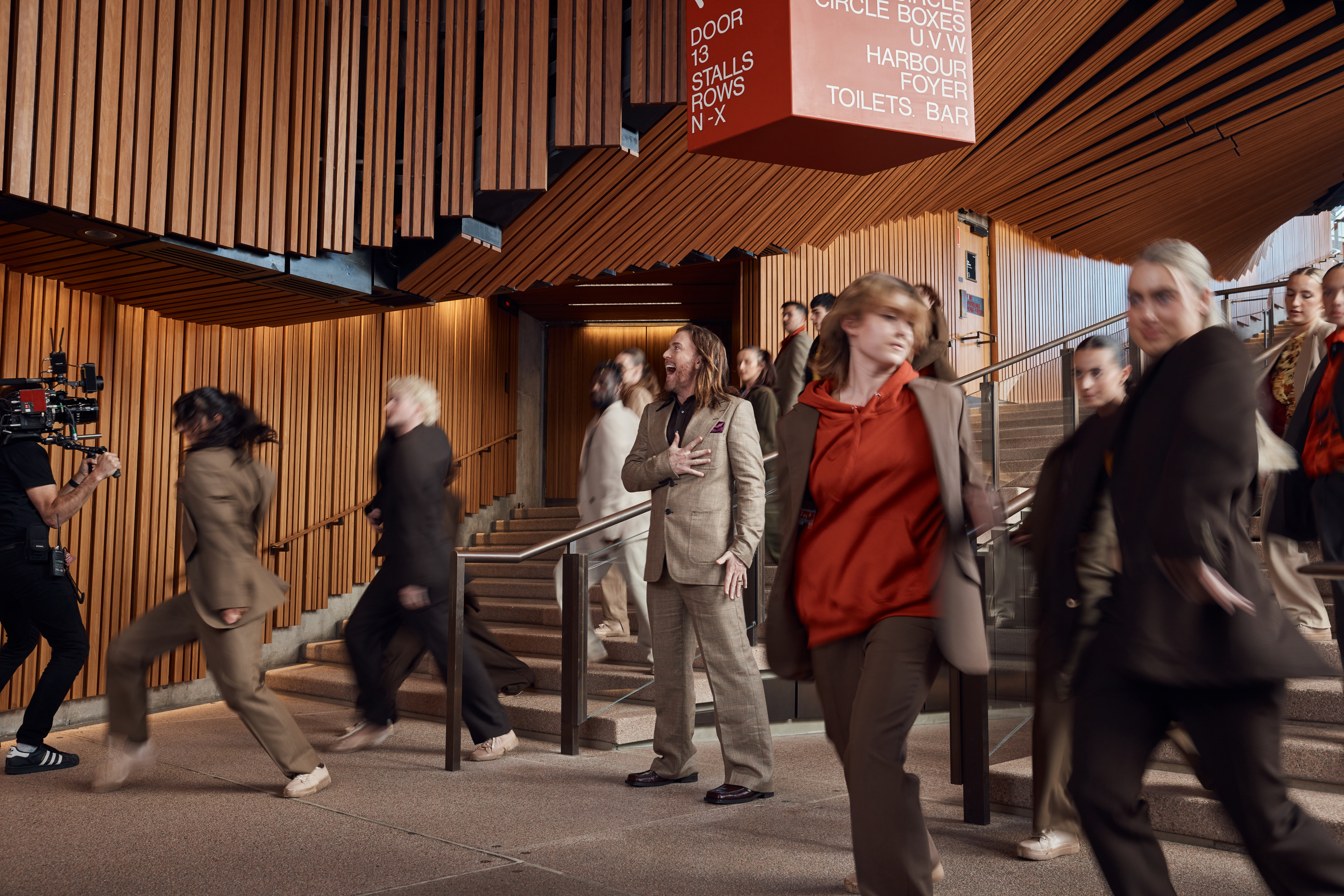 A number of people in brown and grey suiting walking down stairs inside the Opera House.