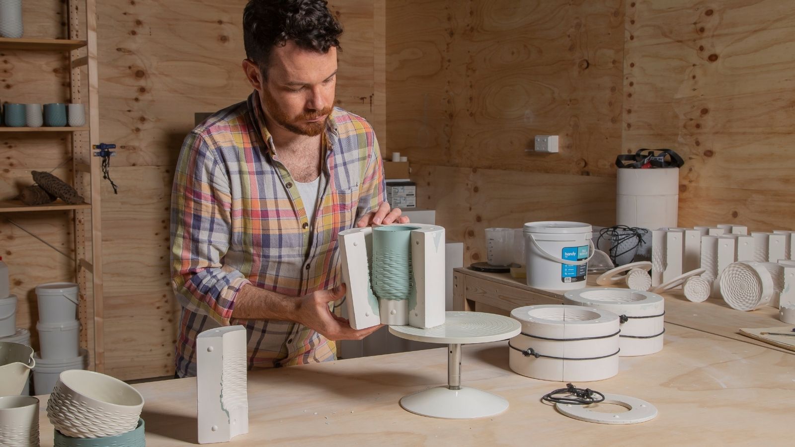 A man in a shirt crafting a blue object in a wooden room.