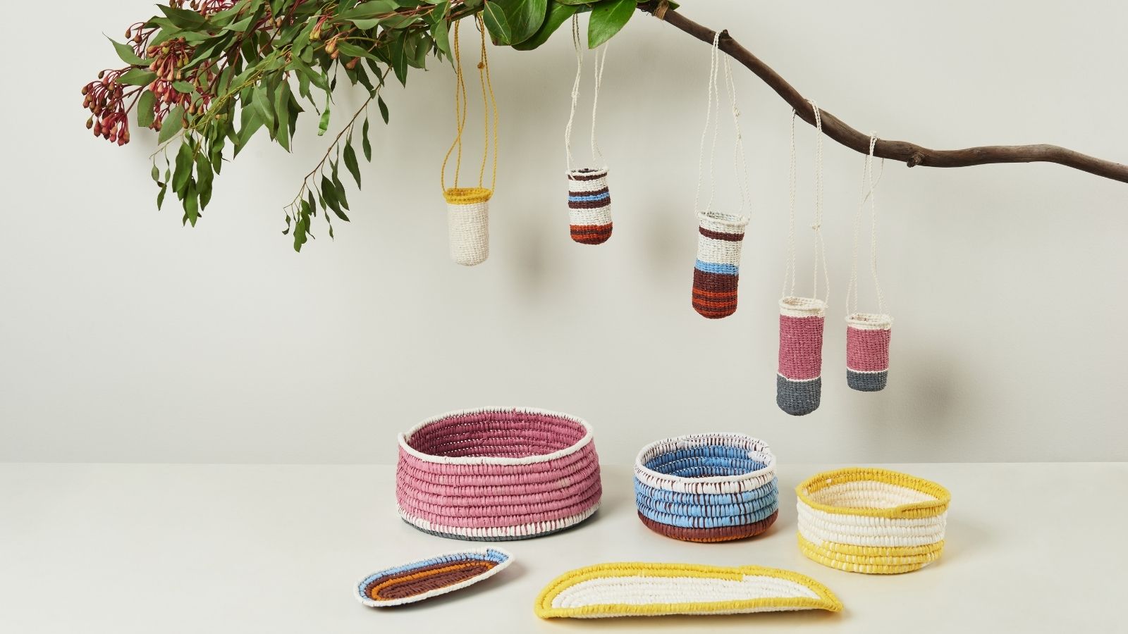 Five knitted buckets hanging off a branch underneath three colored bowls.