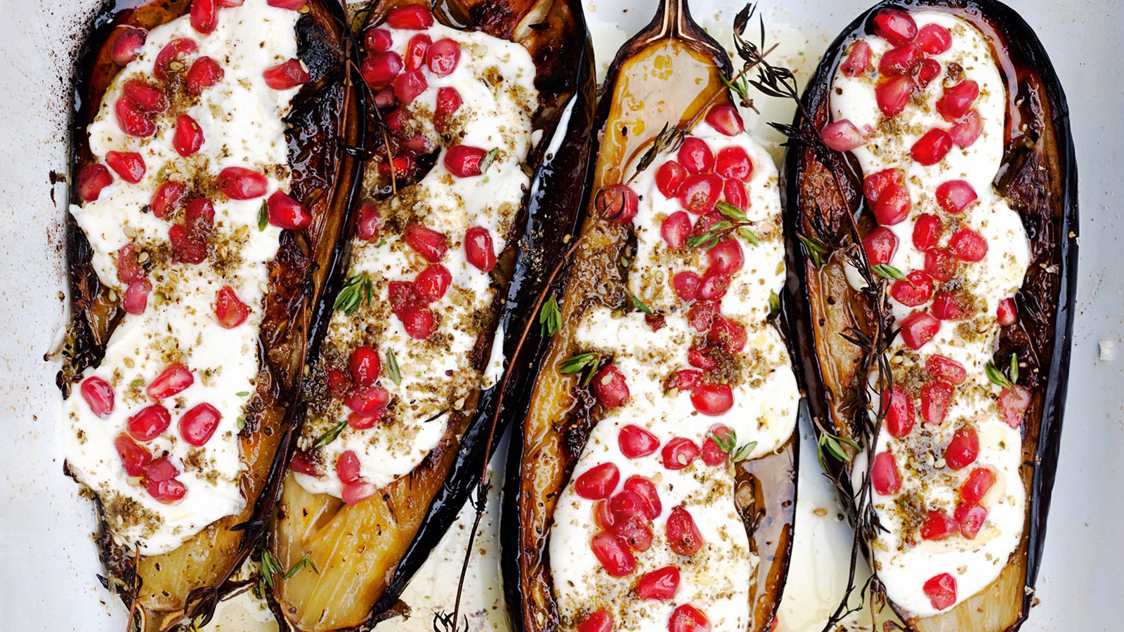 Four roasted vegetables dressed in a white sauce and red fruit on top.