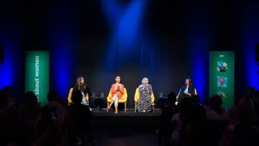 Four women sit on stage clapping.