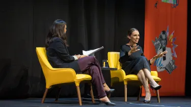 Jacinda Ardern sits and speaks smiling at the audience.