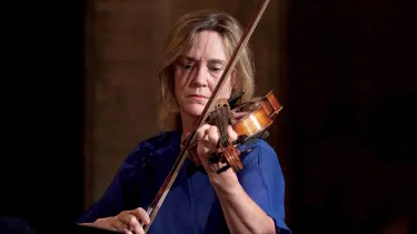A woman in a blue top plays the violin.