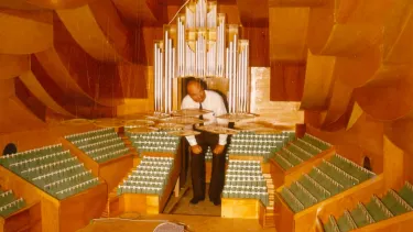 A man stooping under the organ of a large scale model of the Concert Hall, looking at the perspex discs.