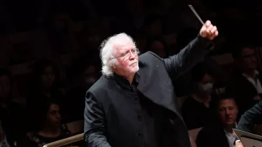 Donald Runnicles stands with his left hand raised as he conducts an orchestra