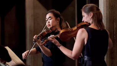 Two female violin players stand playing the violin