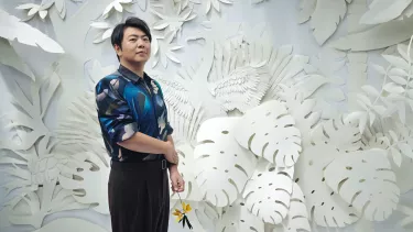 Pianist Lang Lang stands in front of a wall with an intricate cutout forest design