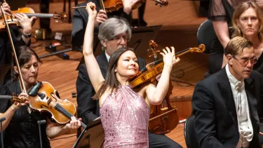 Violinist Arabella Steinbacher in a pink sequin dress flourishes the violin in front of the Sydney Symphony Orchestra violin section
