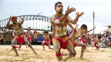 Men in sand pit performing indigenous dance in the homeground of Sydney opera house.