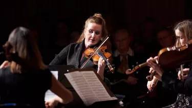 A female violinist plays the violin in front of a Chamber Orchestra
