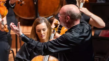 Stephen Layton conducts an Orchestra with arms outstretched