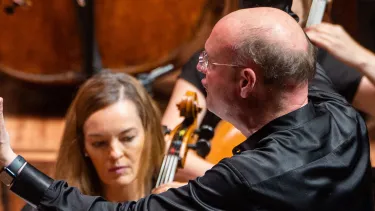 Stephen Layton conducts an Orchestra with arms outstretched
