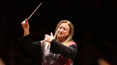 Simone Young conducts with baton in the hand in front of an orchestra