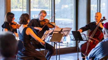 Three violin players stand playing the violin in the Sydney Opera House Utzon Room with a cellist